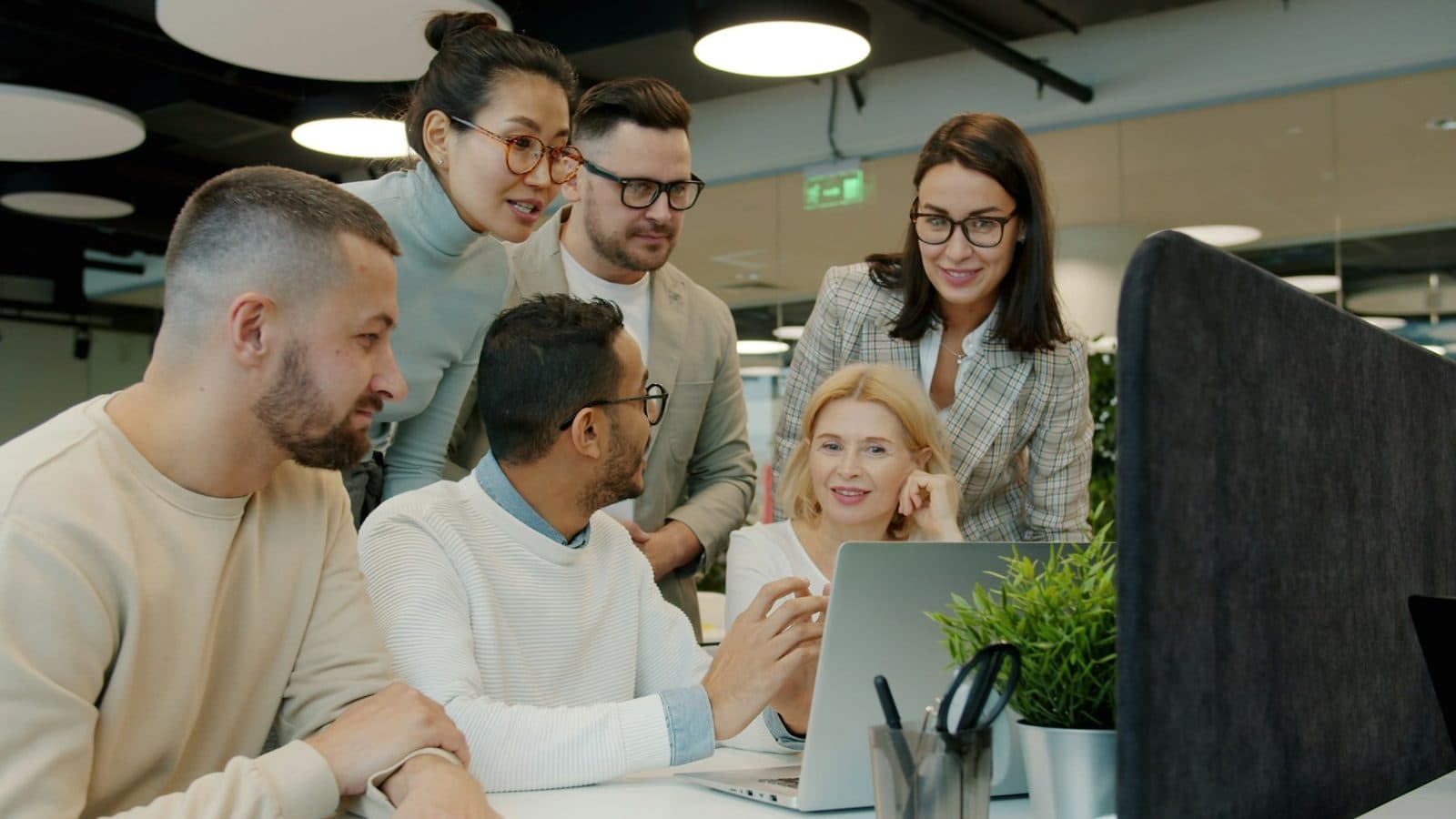 Colleagues gathered around a laptop in an office, working through what is on the screen together.